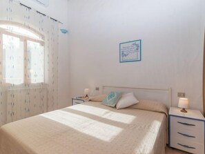 Une chambre à coucher comprenant un lit, deux tables de chevet, une fenêtre avec des rideaux et un élément décoratif mural.