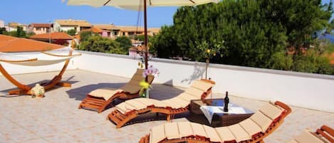 A rooftop terrace with sun loungers, a hammock, and a large umbrella providing shade.