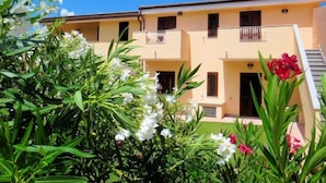 A two-story building with balconies and a small garden area with white and red flowers. - Apartment K Plus by Interhome (Valledoria)
