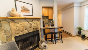 Una sala de estar con chimenea de piedra, un área de cocina con armarios de madera y un taburete de bar.