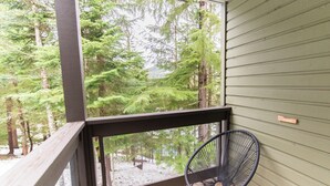 Un balcón con vistas a un bosque, una silla y una ventana con pomo de madera.