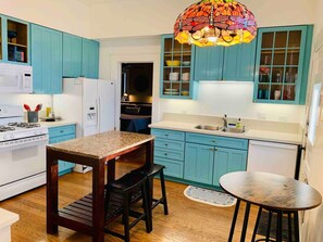 A kitchen with teal cabinets, a granite countertop, a stove, a refrigerator, and a unique stained glass pendant light.