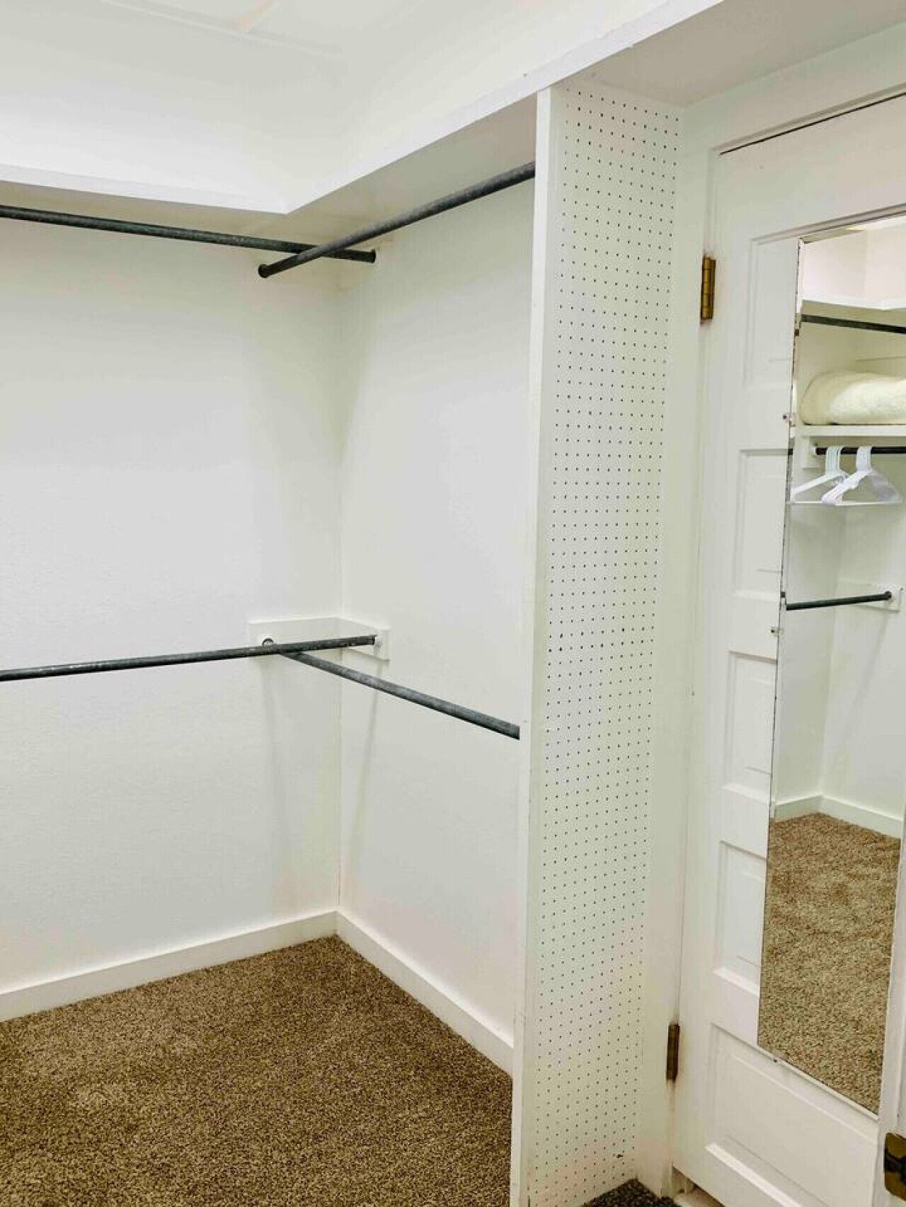A room with a white door, a mirror, a closet with hanging space, and a ceiling-mounted rod.