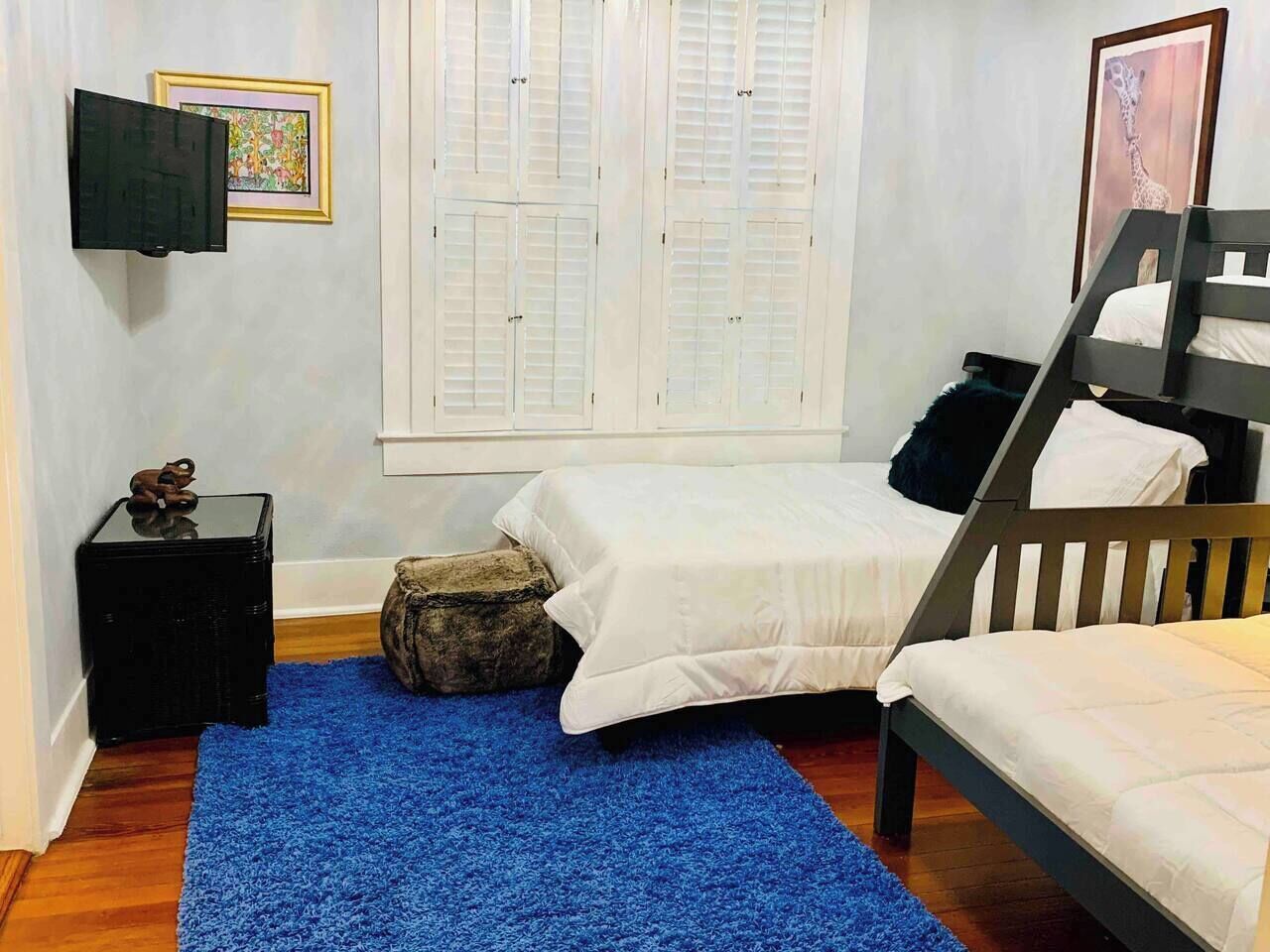 A bedroom with two beds, a blue rug, a small black table, a decorative sculpture, and a window with shutters.