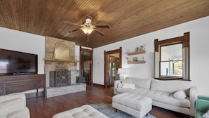 Un salón amplio con techo de madera, chimenea, televisor y un ventanal grande.