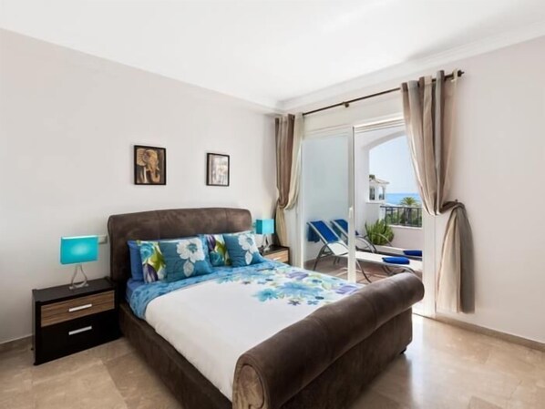 Une chambre à coucher comprenant un lit, une table de chevet, une lampe et donnant sur un balcon avec une chaise.