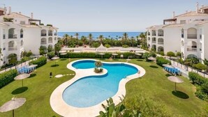 A resort with a central swimming pool, multiple buildings, and a view of the ocean.