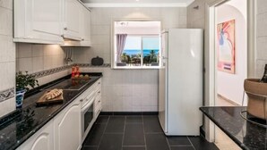 A compact kitchen with white cabinets, a black countertop, and a view of the sea through a window.