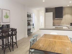 Une cuisine moderne dotée d’une cuisinière intégrée, un coin repas avec une table et des chaises en bois, et une bibliothèque agrémentée d’objets décoratifs.