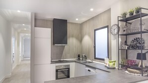 Eine moderne Küche mit Einbauofen, Spüle und Kaffeemaschine. Eine Holzverkleidung und ein Regal mit Dekorationselementen sind ebenfalls vorhanden.