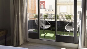 Ein Zimmer mit einer großen Schiebeglasdoor, die auf einen Balkon mit zwei Stühlen und einem kleinen Tisch führt.