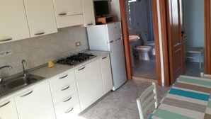 A kitchen with white cabinets, a gas stove, a sink, and a refrigerator. - Holidays in Vieste in charming villas - 4 (Puglia)