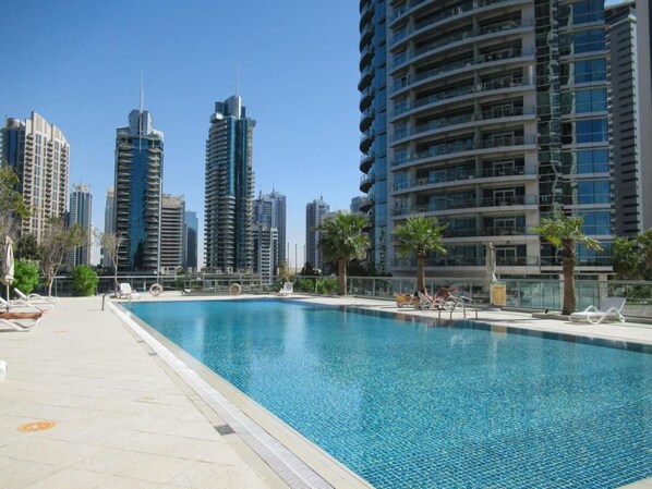 A swimming pool with lounge chairs and palm trees, surrounded by high-rise buildings.