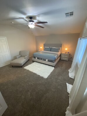 A bedroom with a bed, a chair, a nightstand, a ceiling fan, and a window with blinds.