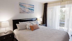 A bedroom with a bed, nightstands, a painting, and a view of the outdoors.