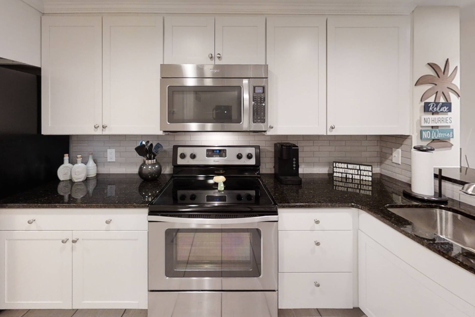 Een moderne keuken met roestvrijstalen apparatuur, witte kasten en een zwart granieten aanrecht.