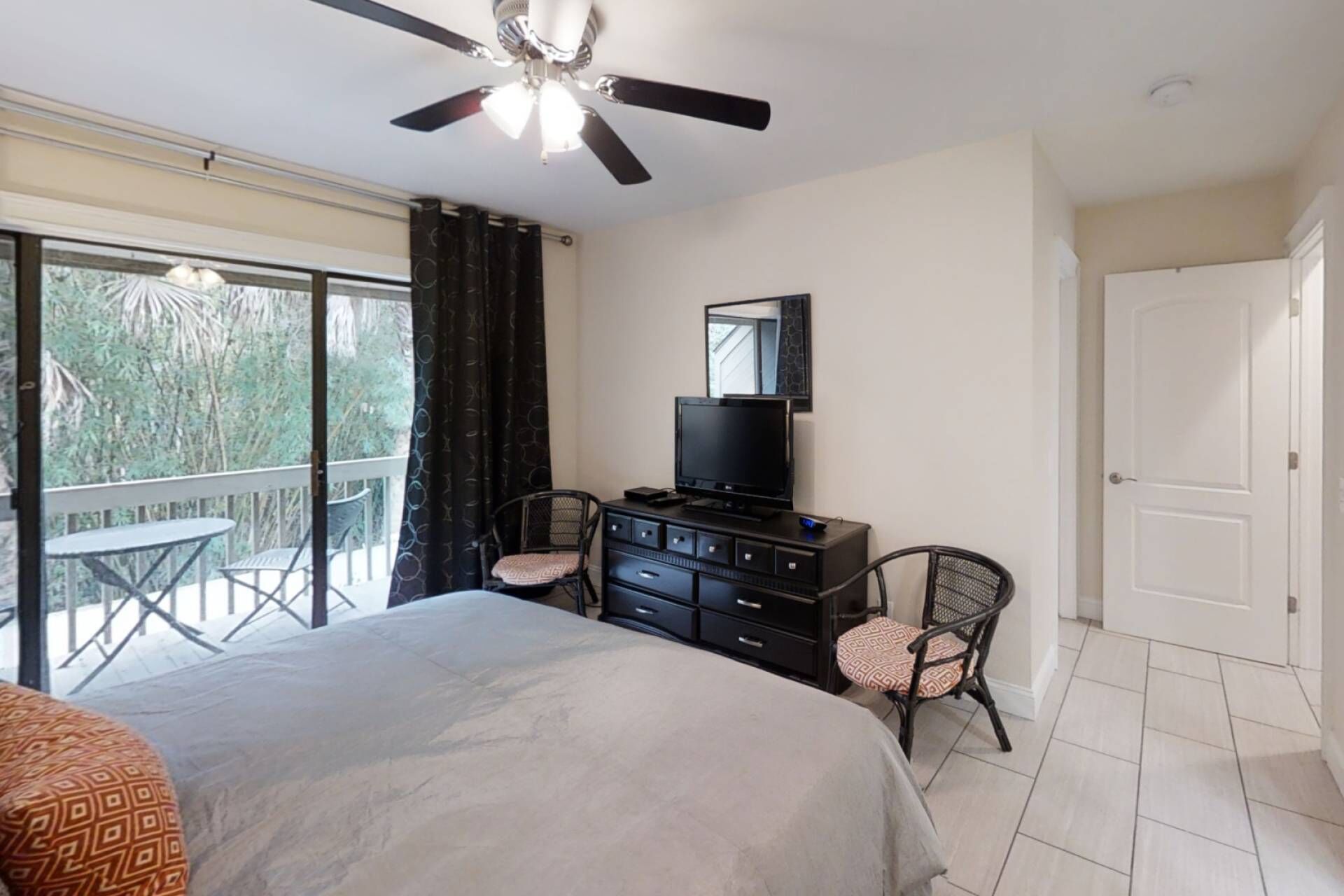 A bedroom with a bed, a TV on a dresser, a ceiling fan, and a balcony with a table and chairs.