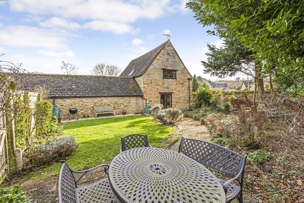 A stone house with a sloped roof, a small lawn, and a metal table with chairs.