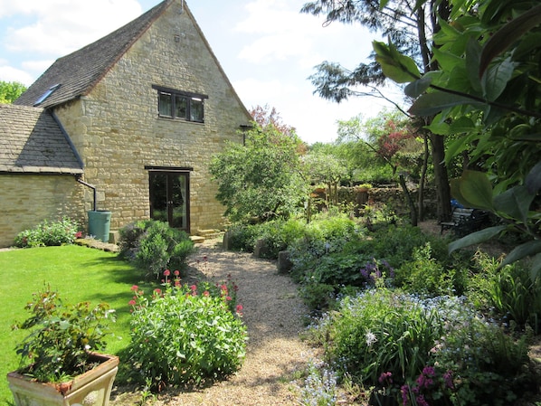 Surrounded by a lush garden, this charming cottage features a sloped roof and a small window.