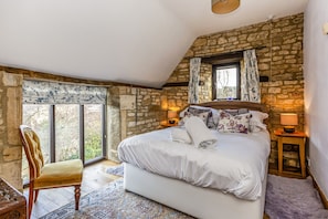 Relax in a charming room with a large window offering a view of the outdoors, a comfortable bed, and a rustic stone wall.
