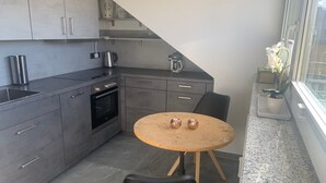 A modern kitchen with grey cabinets, a built-in oven, a coffee maker, and a round wooden table with two chairs. - Modern 50 sqm apartment with living room, bedroom and balcony (Bad Aibling)