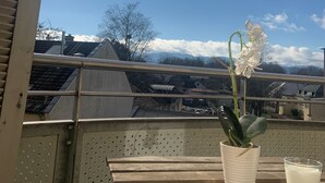 A balcony with a potted orchid, a glass of milk, and a view of buildings and mountains in the background. - Modern 50 sqm apartment with living room, bedroom and balcony (Bad Aibling)