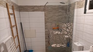 Kylpyhuoneessa on suihku, wc ja pesuallas. Seinää vasten on nojattu tikkaat ja lattialla on sininen ämpäri.