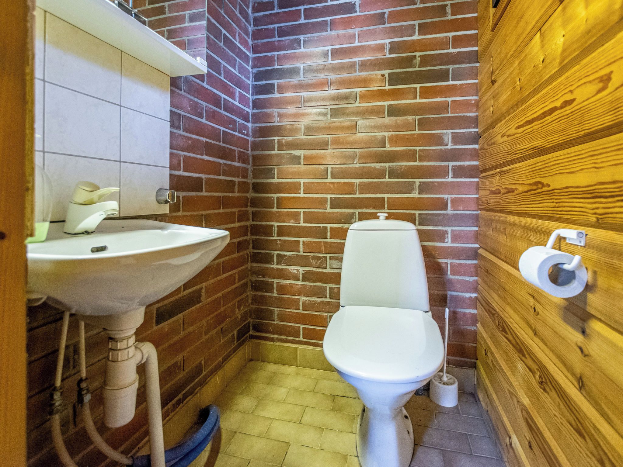 Une petite salle de bain avec un lavabo blanc, des toilettes et un mur en bois.