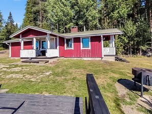 Punainen rakennus, jossa on kuisti, savupiippu ja ruohikkoalue pihalla.