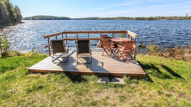 Une terrasse en bois avec quatre chaises et une table, donnant sur un lac.
