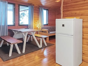 Interior de una cabaña de madera con una mesa de comedor, bancos, un sofá y un refrigerador.