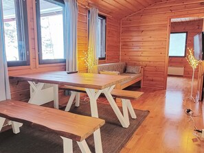 Puinen mökki, jonka sisätiloissa on ruokapöytä, penkit, sohva ja televisio.