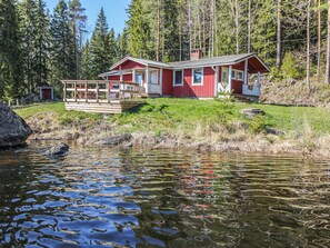 A red cabin with a deck, surrounded by a forest and a lake. - Lahdeke by Interhome (Leppävirta)