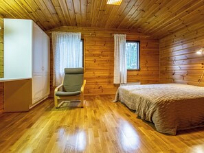 Interior de cabana com cama, cadeira, guarda-roupa e janela.