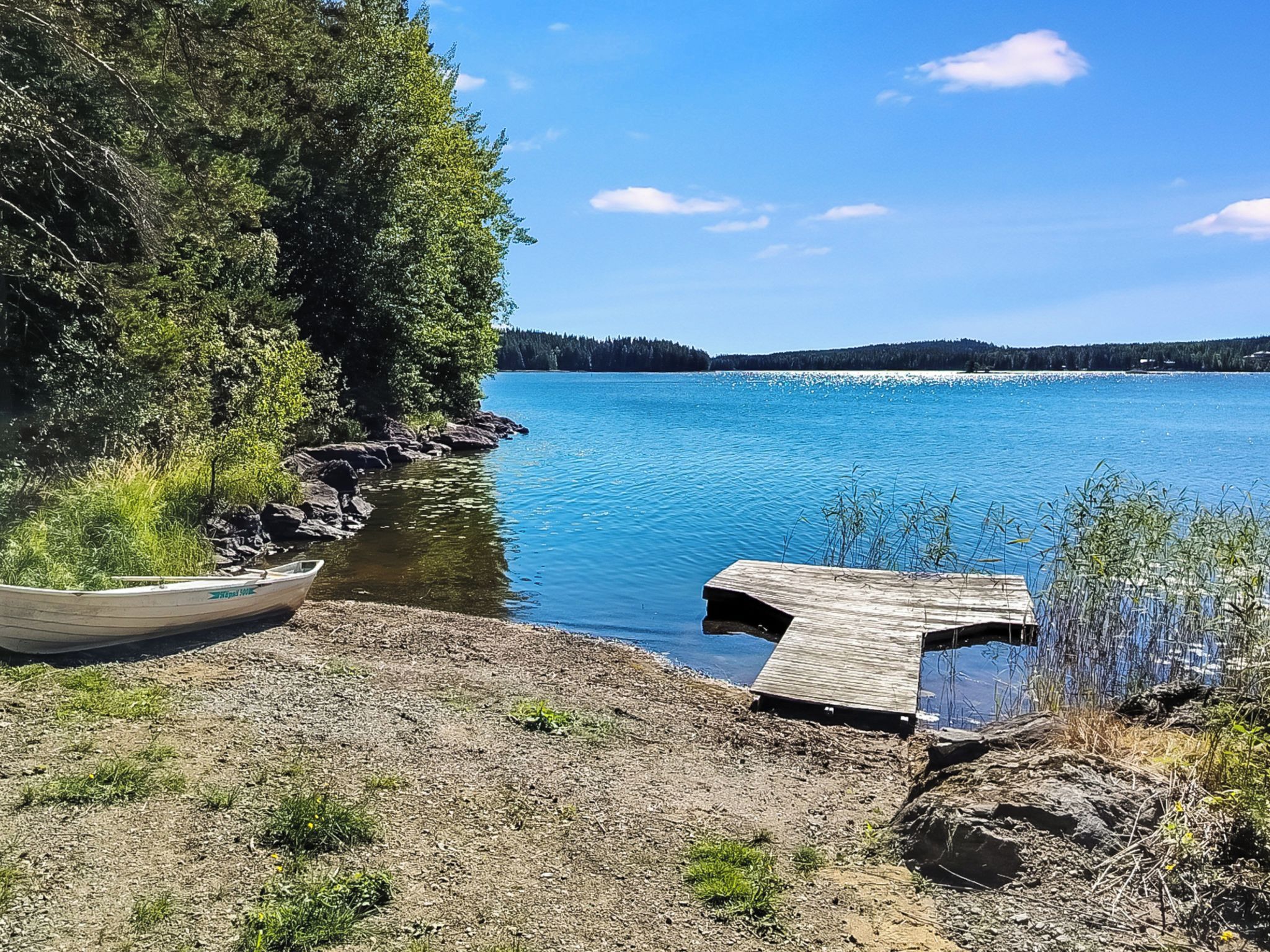 A calm lake with a dock and a boat, surrounded by dense trees and a clear sky.