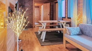 L’intérieur chaleureux d’un chalet avec des murs en bois, une table à manger en bois, des bancs, un canapé et des guirlandes lumineuses décoratives.