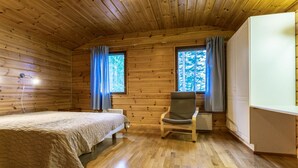 A wooden cabin room with a bed, a chair, and a desk.