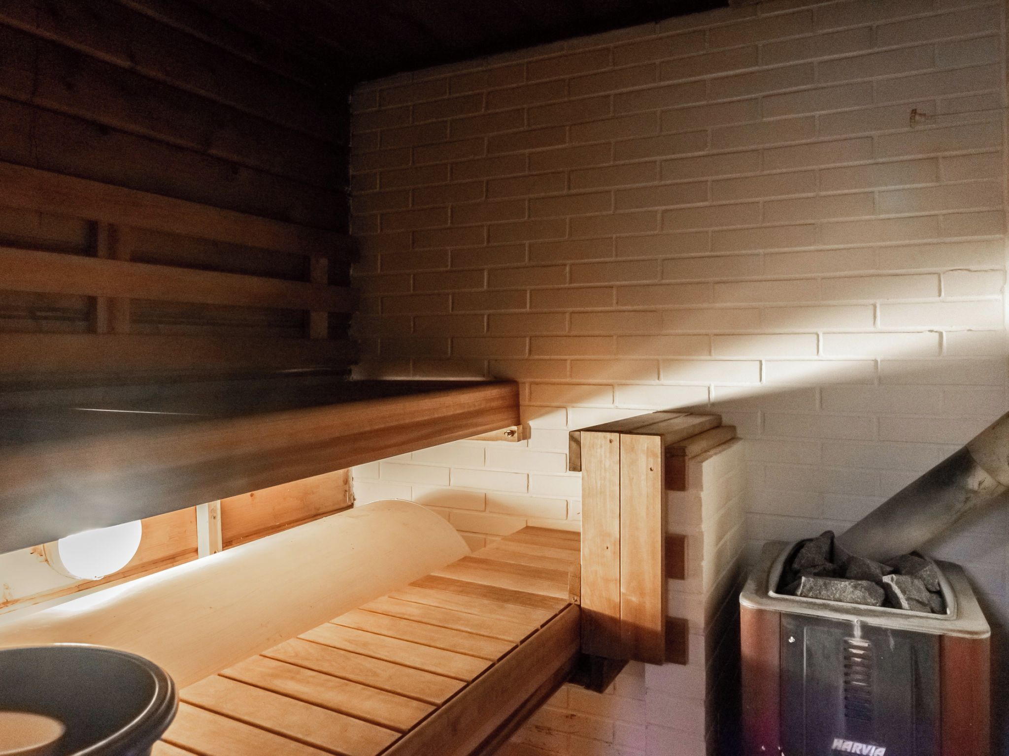 A sauna room with wooden benches, a brick wall, and a Harvia sauna heater.