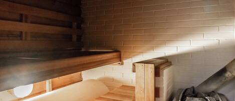 A sauna room with wooden benches, a brick wall, and a Harvia sauna heater.