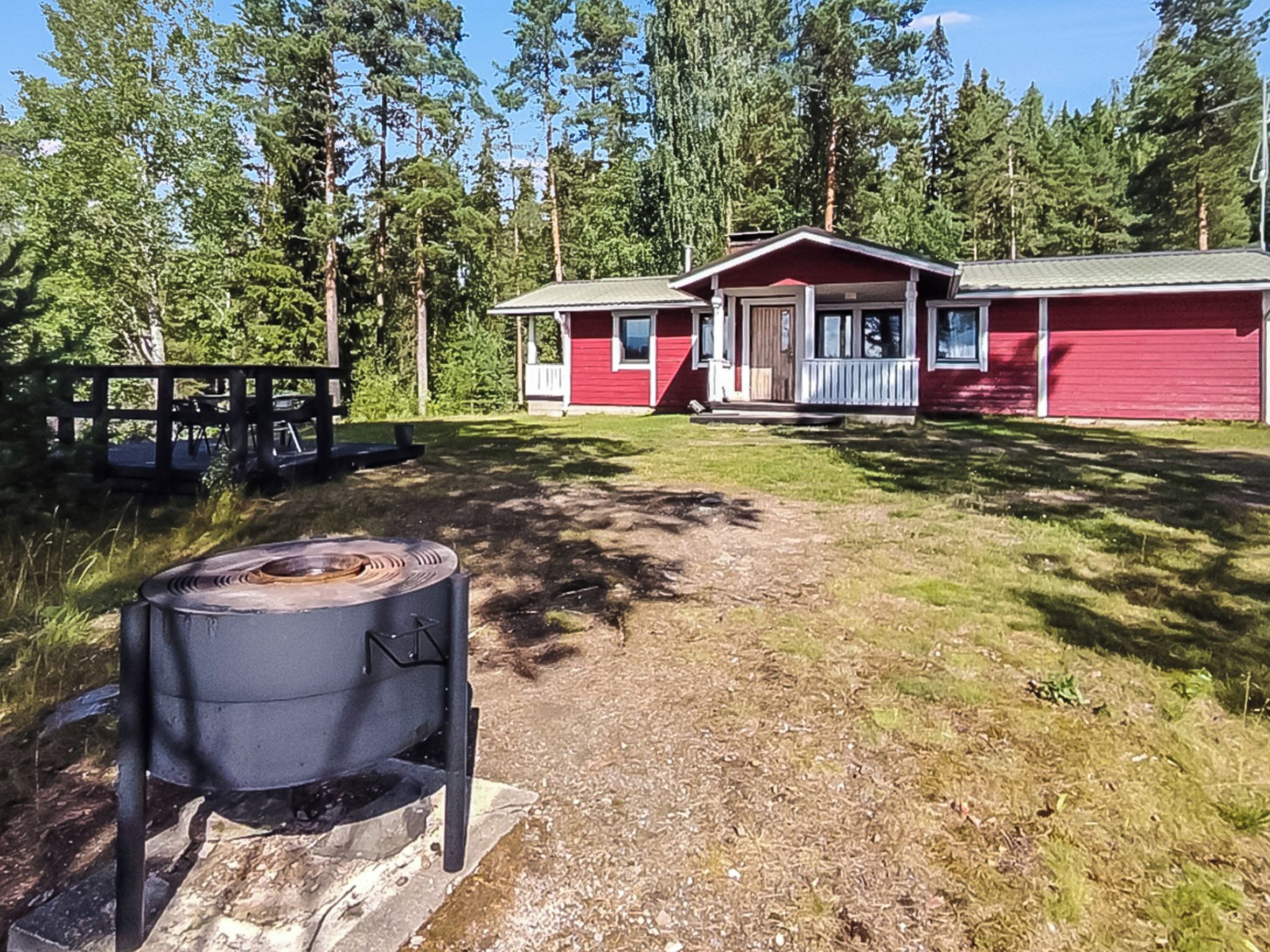 Punainen mökki, jossa on kuisti, grilli ja puinen terassi.
