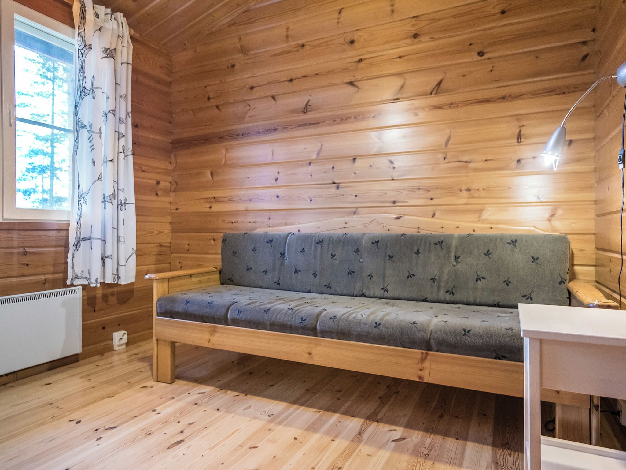 Een houten chalet van binnen met een bank, een raam met gordijnen en een radiator.