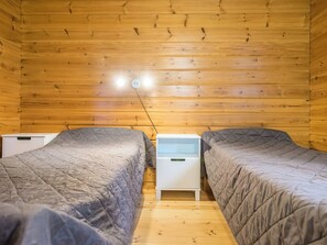 Una cabaña con dos camas, una mesita de noche pequeña y techo de madera.