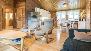 Hyggelig hyttekrog med trævægge, en stensokkel og spise- samt opholdsområde med sofa og stole.