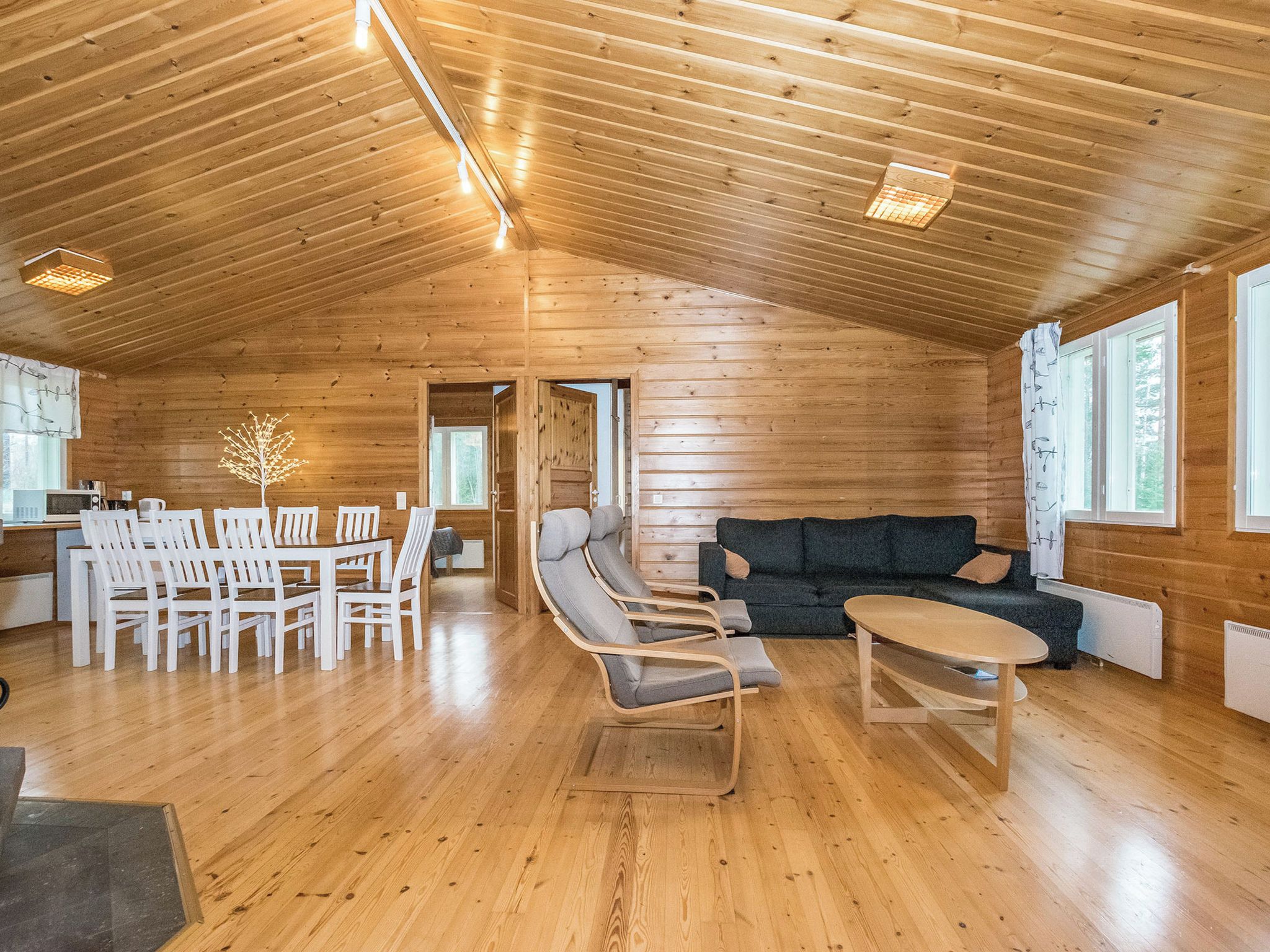 A spacious wooden interior with a dining area, seating, and a view through a doorway.