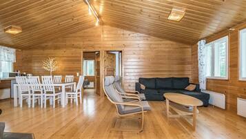 A spacious wooden interior with a dining area, seating, and a view through a doorway.