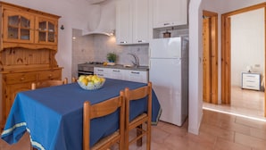 A compact kitchen with wooden cabinets, a white refrigerator, and a dining table with a blue tablecloth. - Vacation home A 1 by Interhome (Valledoria)