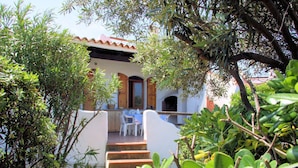 A white building with a red-tiled roof, a wooden door, and a small outdoor seating area with a table and chairs. - Vacation home A 1 by Interhome (Valledoria)