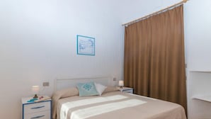 A bedroom with a bed, two bedside tables, a nightstand, a wall-mounted picture, and a window with curtains. - Vacation home A 1 by Interhome (Valledoria)