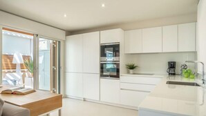 Una cocina moderna con armarios blancos, horno empotrado y cafetera.
