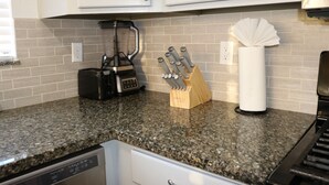 Une cuisine dotée de plans de travail en granit, d’un mixeur, d’un bloc à couteaux et d’un porte-rouleau d’essuie-tout.